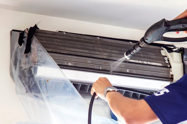 The technicians are cleaning the air conditioner by spraying water. Hand and water spray are cleaning the air conditioner on white background.